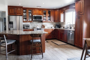A kitchen with wooden cabinets, stainless steel appliances, and a large island with bar stools. - Stardust Borrego — Movie Lounge + Bar • Fire Pit • AC • Pet-Friendly Retreat (Borrego Springs)