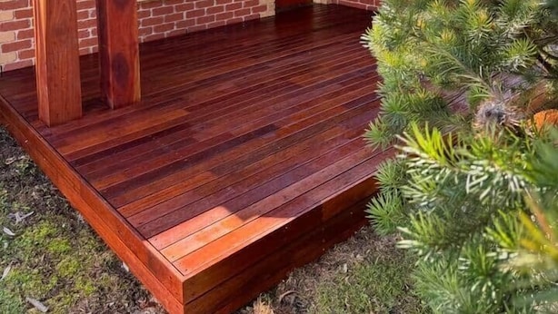 Een klein huis van baksteen met een houten terras, een raam en een deur.