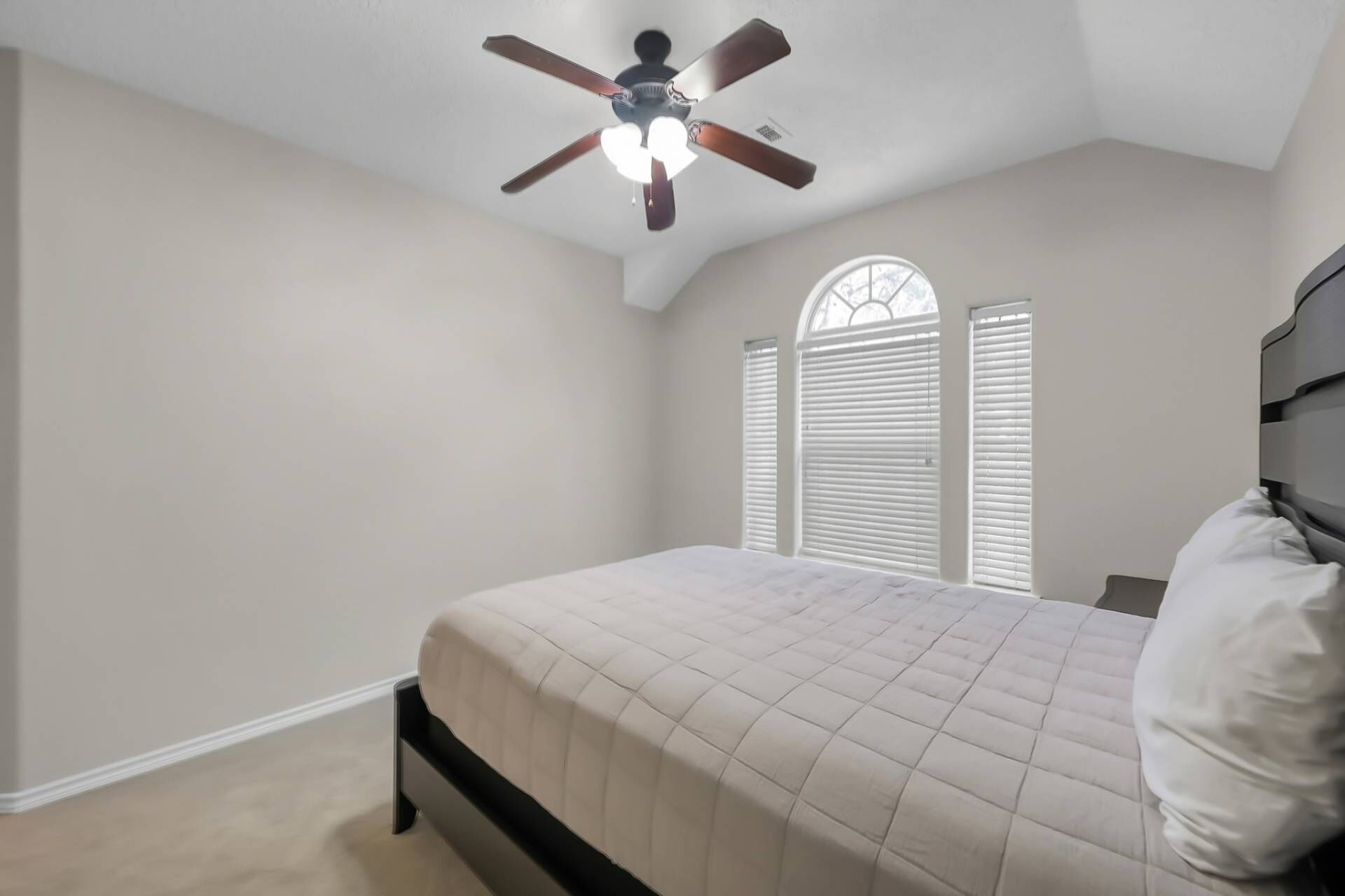 A bedroom with a bed, a ceiling fan, and a window with blinds.