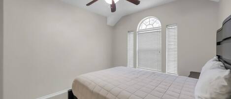 A bedroom with a bed, a ceiling fan, and a window with blinds.