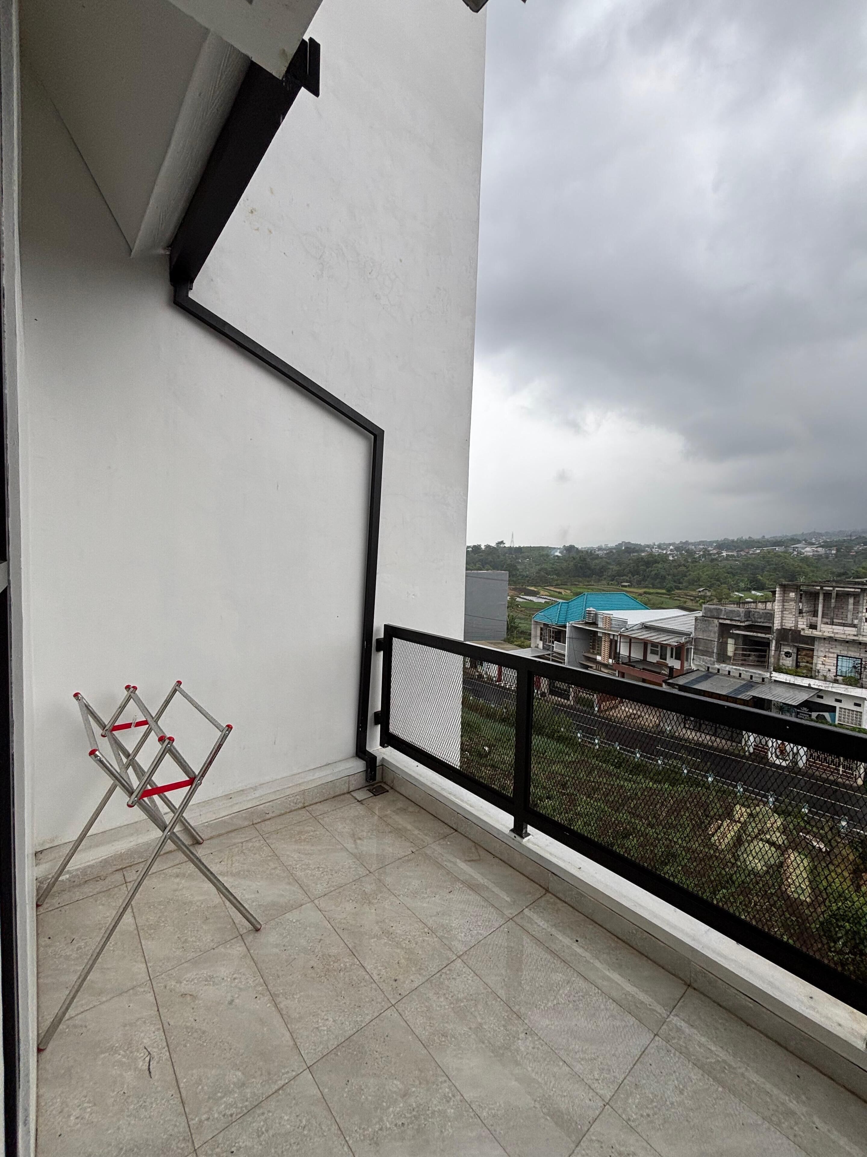 A balcony with a metal ladder leaning against the wall, a tiled floor, and a view of buildings and greenery in the distance.