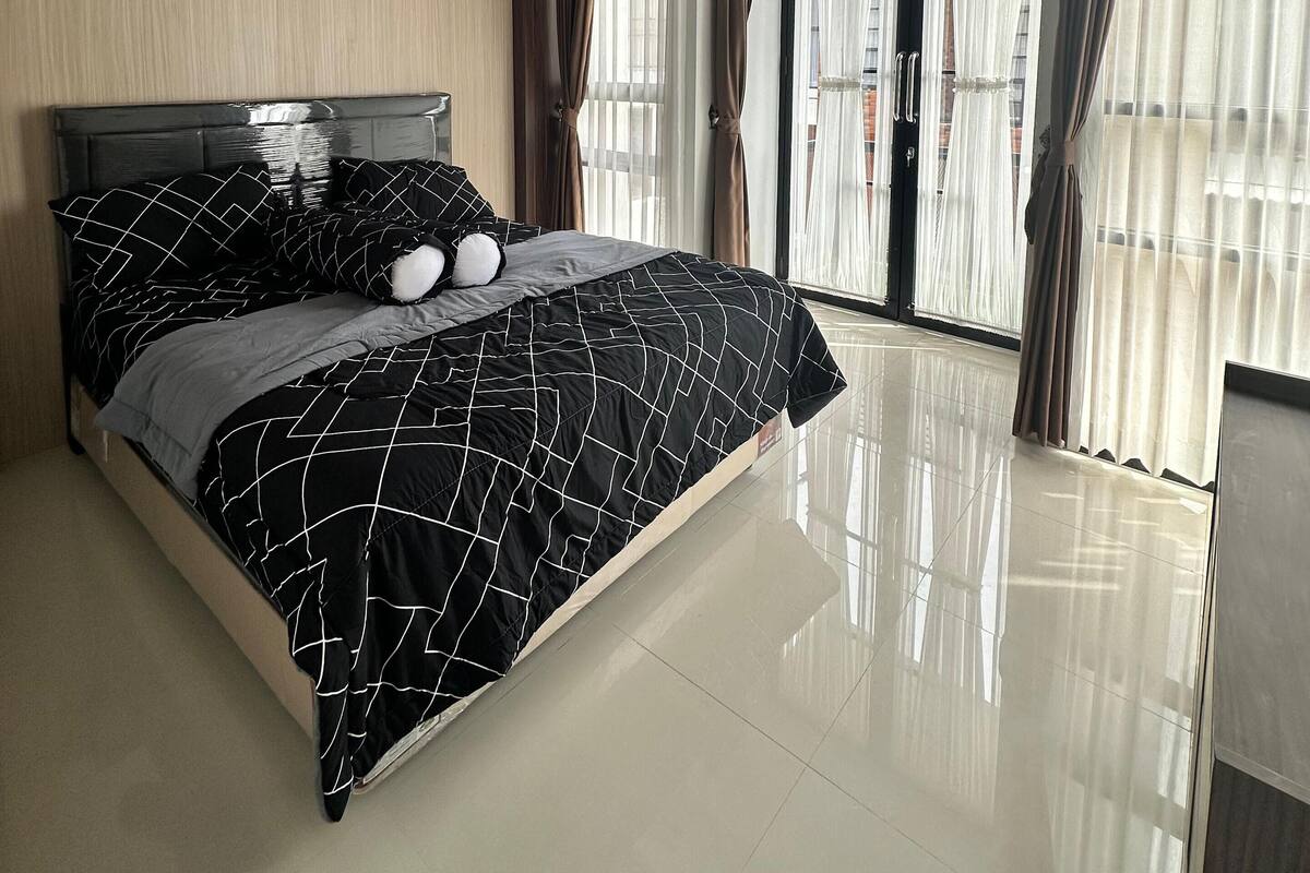 A modern bedroom with a large bed, a wooden ceiling, and a view of the city through large windows.