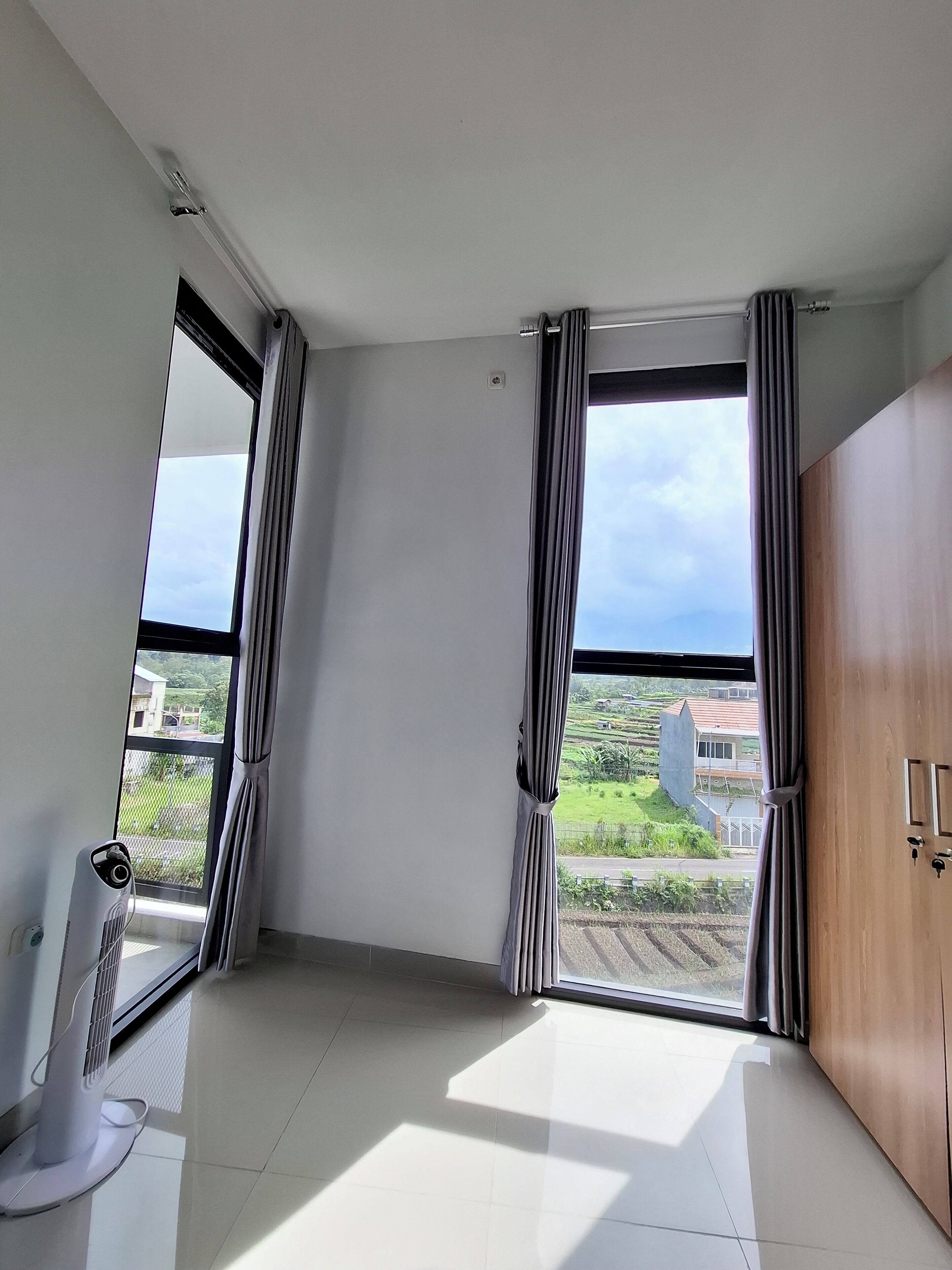 A room with large windows, a radiator, and a white ceiling fan.