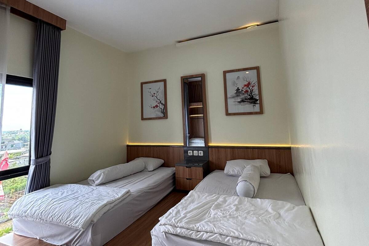 A hotel room with two single beds, a wooden platform, a nightstand with a mirror, and framed artwork on the wall.