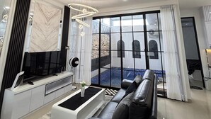 A modern living room with a sofa, TV, and a view of a courtyard. - Athara Residence (Batu)
