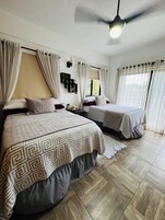 Un dormitorio con dos camas, ventilador de techo y ventana con cortinas.
