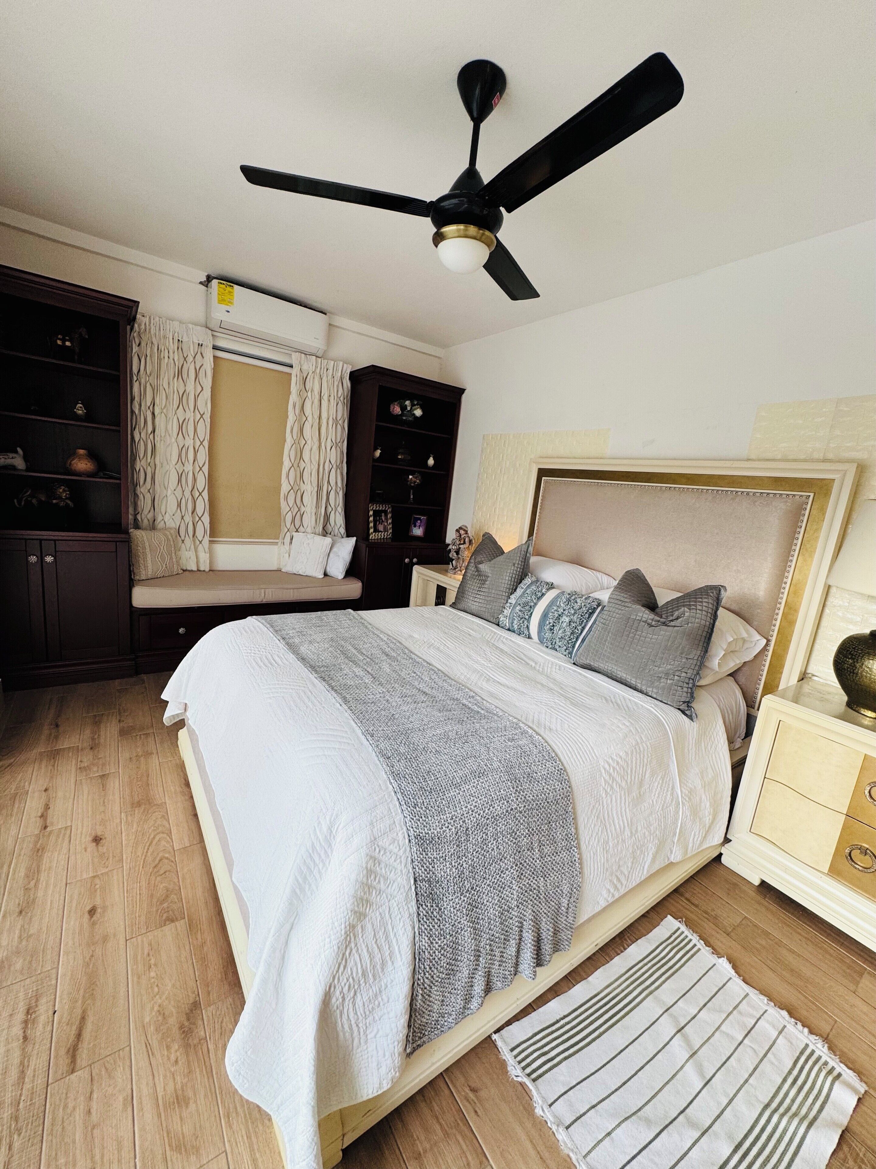 A bedroom with a bed, a nightstand, a dresser, a ceiling fan, and a window with curtains.