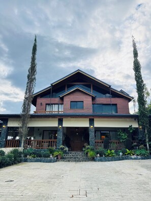 A two-story house with a front porch, stone steps, and a garden with various plants. - Luxury Mountain Villa w Pool & Fire Pits (Jarabacoa)