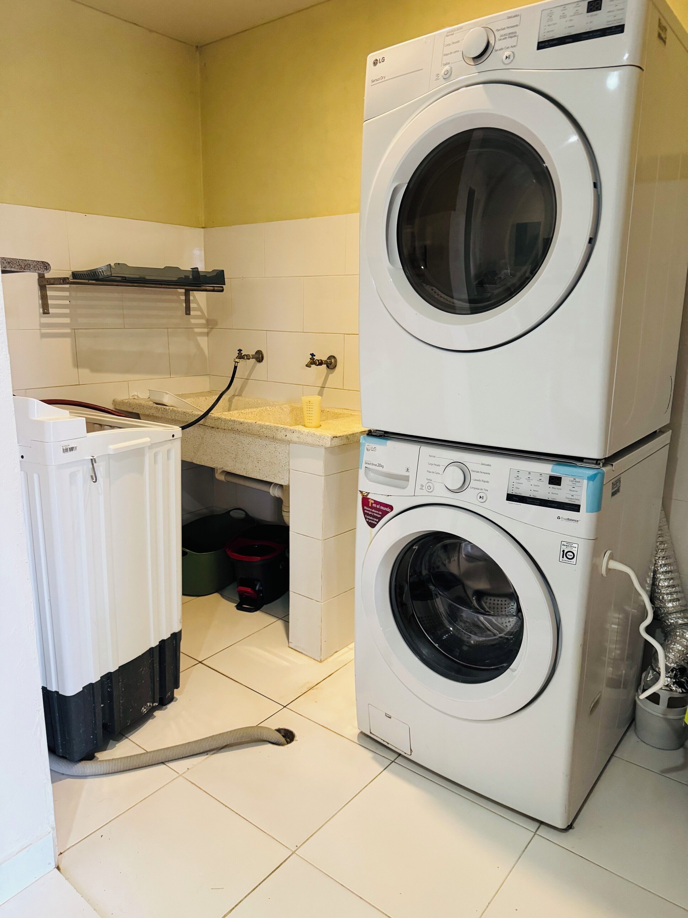 Une buanderie équipée d’un lave-linge et d’un sèche-linge superposés, d’un petit évier et d’un tuyau d’eau.