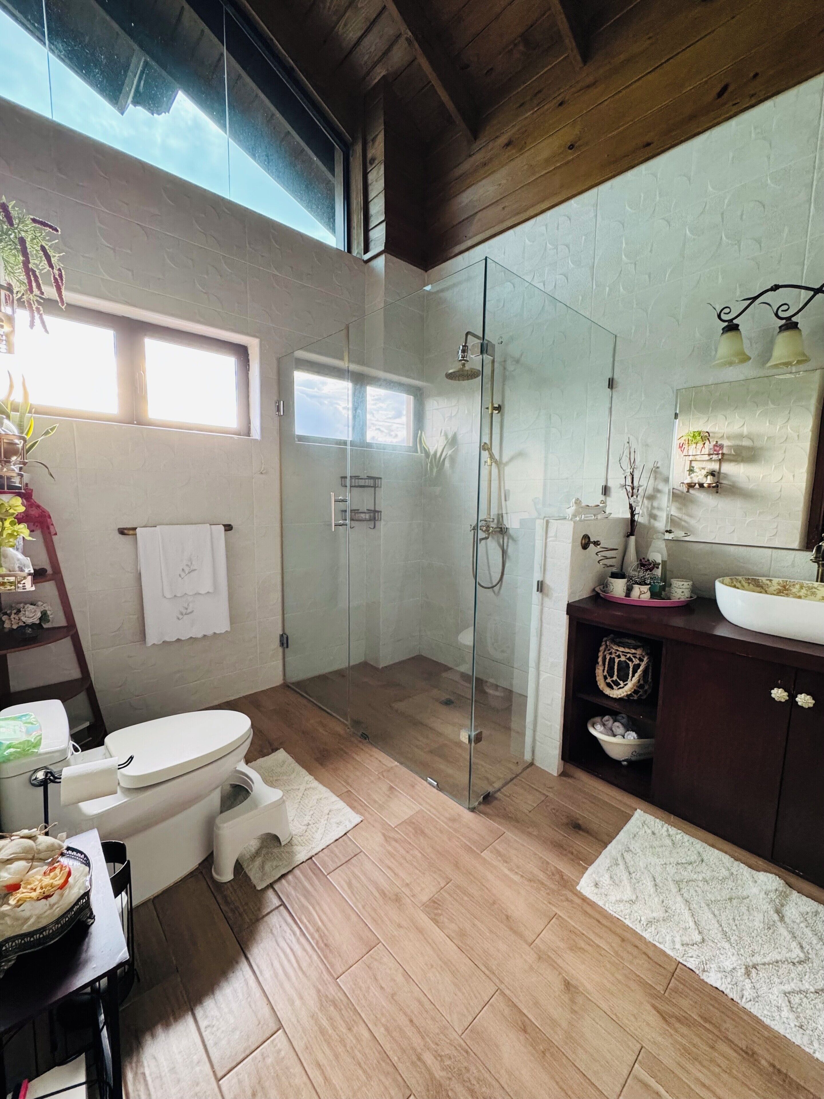 Un baño moderno con ducha de vidrio, inodoro blanco y tocador de madera con lavamanos grande.