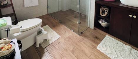 Un baño moderno con ducha de vidrio, inodoro blanco y tocador de madera con lavamanos grande.
