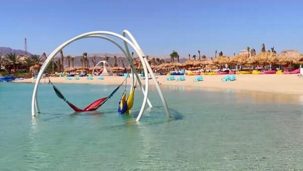 Una playa con aguas cristalinas, una hamaca y sillas.