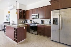 A kitchen with wooden cabinets, a stainless steel refrigerator, a stove, and a microwave. - 432 Two Bedroom Ocean View Vivo Resorts (Bajos de Chila)