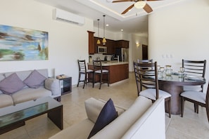 A living room with a sofa, a coffee table, and a dining area with a table and chairs. There is a kitchen in the background with a refrigerator and a sink. - 432 Two Bedroom Ocean View Vivo Resorts (Bajos de Chila)
