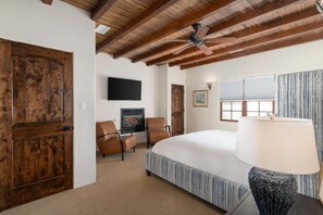 A bedroom with a large bed, a ceiling fan, a fireplace, and a television. - Sagebrush Casita: 2bd/2.5bth Historic Property Close to Plaza (Santa Fe)