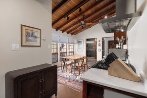 A kitchen with a wooden ceiling, a dining area with a table and chairs, and a kitchen counter with a knife block. - Sagebrush Casita: 2bd/2.5bth Historic Property Close to Plaza (Santa Fe)