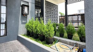 Un patio exterior moderno con piso de baldosas, plantas en macetas y una manguera azul.