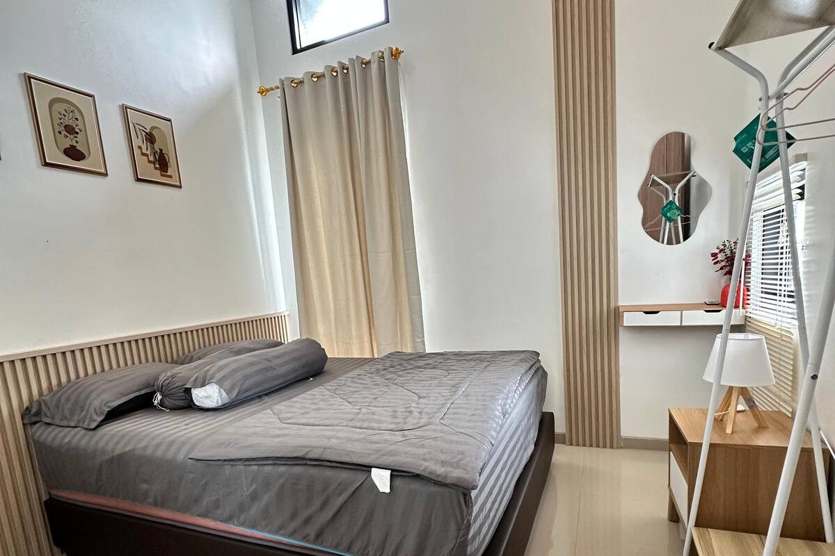 A neatly arranged bedroom with a bed, a bedside table, a lamp, and a window with curtains.