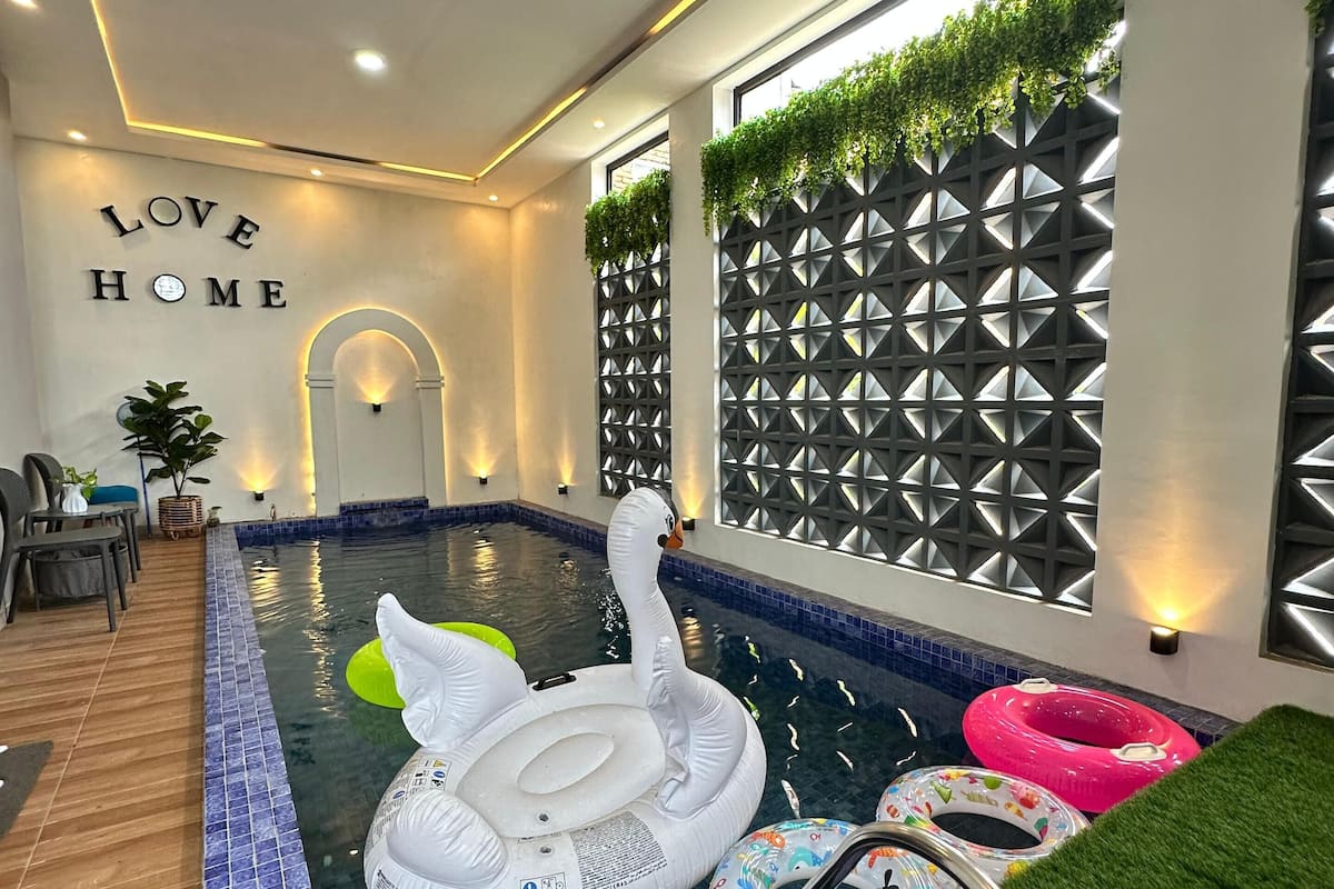 An indoor swimming pool with a swan inflatable, colorful swim rings, and a 'LOVE HOME' sign.