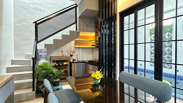 Un comedor moderno con una mesa de vidrio, dos sillas tapizadas en azul y un jarrón con flores.