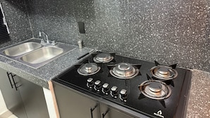 Une cuisine dotée d’un plan de travail en granit, d’un évier en acier inoxydable et d’une cuisinière noire à quatre brûleurs.