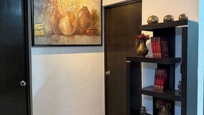 Un couloir avec un tableau encadré, une bibliothèque remplie de livres et d’objets décoratifs, et une porte.