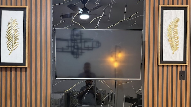 Un salon moderne doté d’un grand téléviseur à écran plat fixé sur un mur en bois, d’un ventilateur de plafond et d’œuvres d’art encadrées de part et d’autre.
