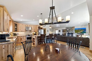 A spacious kitchen with wooden cabinets, a dining area with a large wooden table, and a living room with a fireplace and a television.