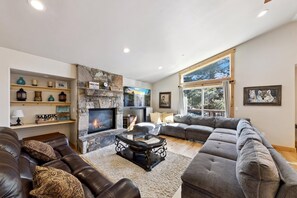 A living room with a stone fireplace, a large grey sectional sofa, a glass coffee table, and a television.