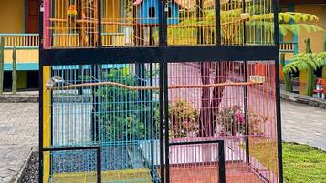 A multi-level birdcage structure with various compartments, set against a backdrop of a clear sky and tropical vegetation.