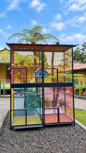 A multi-level birdcage structure with various compartments, set against a backdrop of a clear sky and tropical vegetation. - Onsen Resort kaliurang (Pakem)