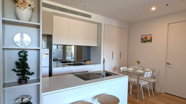 Una cocina moderna con armarios blancos, una isla central con taburetes y un comedor con mesa y sillas.