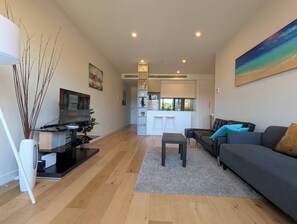 A modern living room with a sofa, a coffee table, and a TV on a stand. There is a kitchen area with a bar and stools in the background. - Balwyn Bright Beauty|Balcony|Parking|Walk to Shops (Balwyn North)