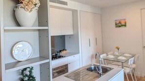 Una cocina moderna con armarios blancos, un lavamanos de acero inoxidable y una zona de comedor con una mesa y sillas de vidrio.