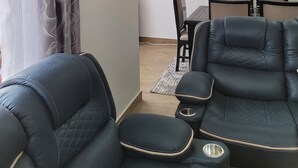 Olohuone, jossa on sohva, ruokapöytä tuoleineen ja seinälle kiinnitetty hylly.