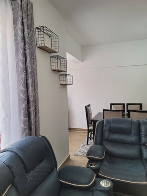 A living room with a sofa, a dining table with chairs, and a wall-mounted shelf. - Phenomenal 3-bedroom/DSQ apartment in vibrant Nairobi neighborhood (Nairobi)