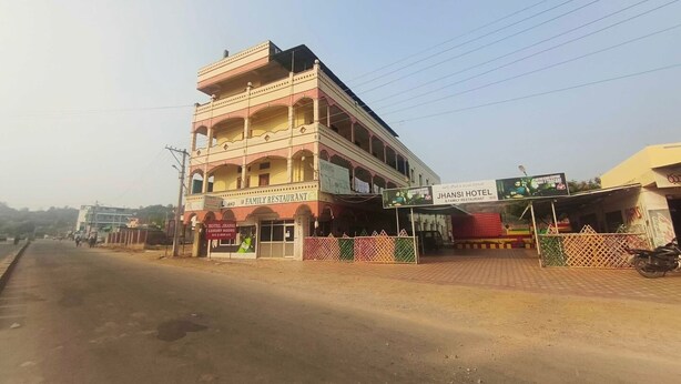 Un hotel de varios pisos con balcones, un restaurante familiar y un letrero que dice 'JHANSI HOTEL & FAMILY RESTAURANT'.