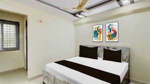 Un dormitorio con cama, ventilador de techo y dos cuadros abstractos en la pared.