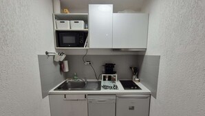 Eine kompakte Küchenzeile mit Mikrowelle, Kaffeemaschine und kleinem Kühlschrank.