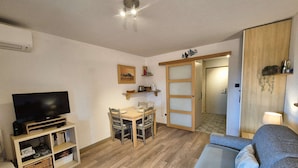 Ein gemütlicher Wohnraum mit Flachbildfernseher, einem Esstisch mit Stühlen, einer Couch und einem Holzschrank.