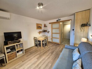 A compact living space with a flat-screen TV, a dining table with chairs, a sofa, and a wooden cabinet. - 1-bedroom, Wi-Fi, walking distance to the beach (ST MANDRIER SUR MER)
