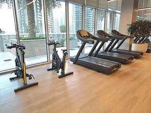 A gym with exercise equipment, large windows, and a view of palm trees and buildings. - Skyline Burj  Views at Forte Tower 2, Walk to Dubai Mall, Sleeps 12 (Dubai)