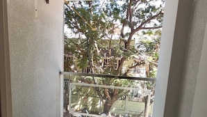 A narrow balcony with a metal railing, a tree, and a view of a residential area. - Jyothis living spaces (Bengaluru)