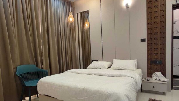 A modern bedroom with a large bed, a nightstand, a chair, and a decorative wall panel. - Jyothis living spaces (Bengaluru)