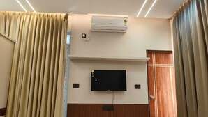 A hotel room with a mounted air conditioner, a flat-screen TV, and a wooden wardrobe. - Jyothis living spaces (Bengaluru)