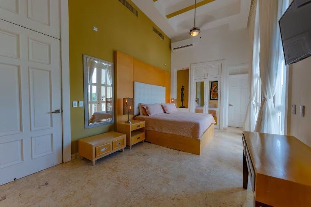 A bedroom with a bed, bedside tables, a mirror, and a TV.