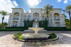 A large, multi-story building with a central fountain, surrounded by palm trees and a cobblestone courtyard. - Paradise Hills Mansion (Puerto Plata)