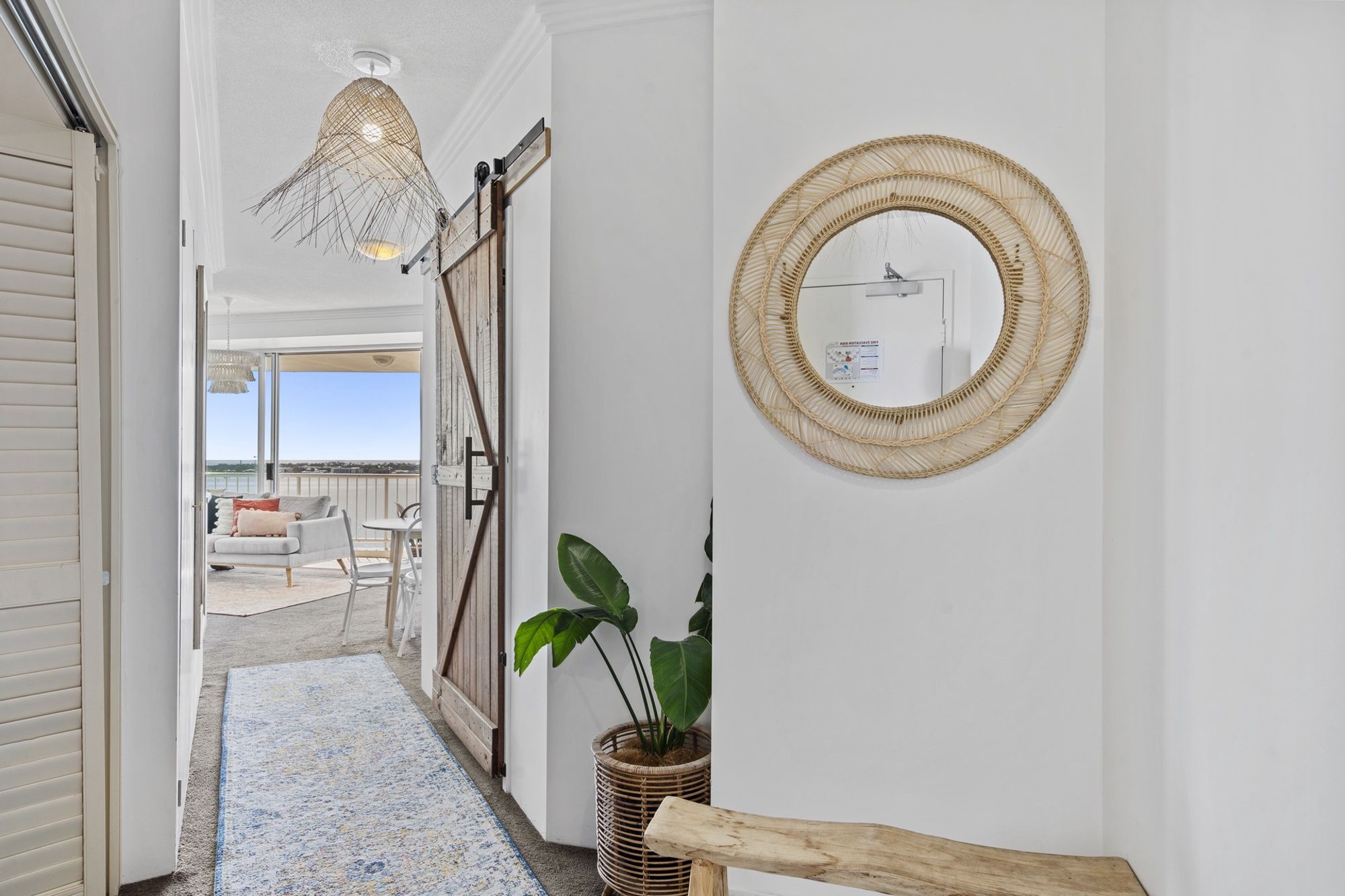 A hallway with a view to a balcony, a wicker mirror, and a hanging light fixture.