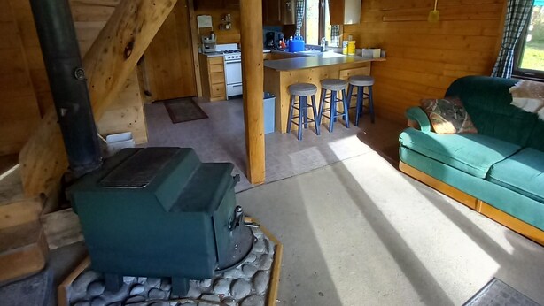 Ein rustikales Blockhaus-Interieur mit Kamin aus Stein, Holzbalken, einer Küchenzeile und einem blaugrünen Sofa.