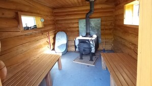 Ein Holzblockbau-Innenraum mit einem zentralen Holzofen, Bänken und einem Teppich.
